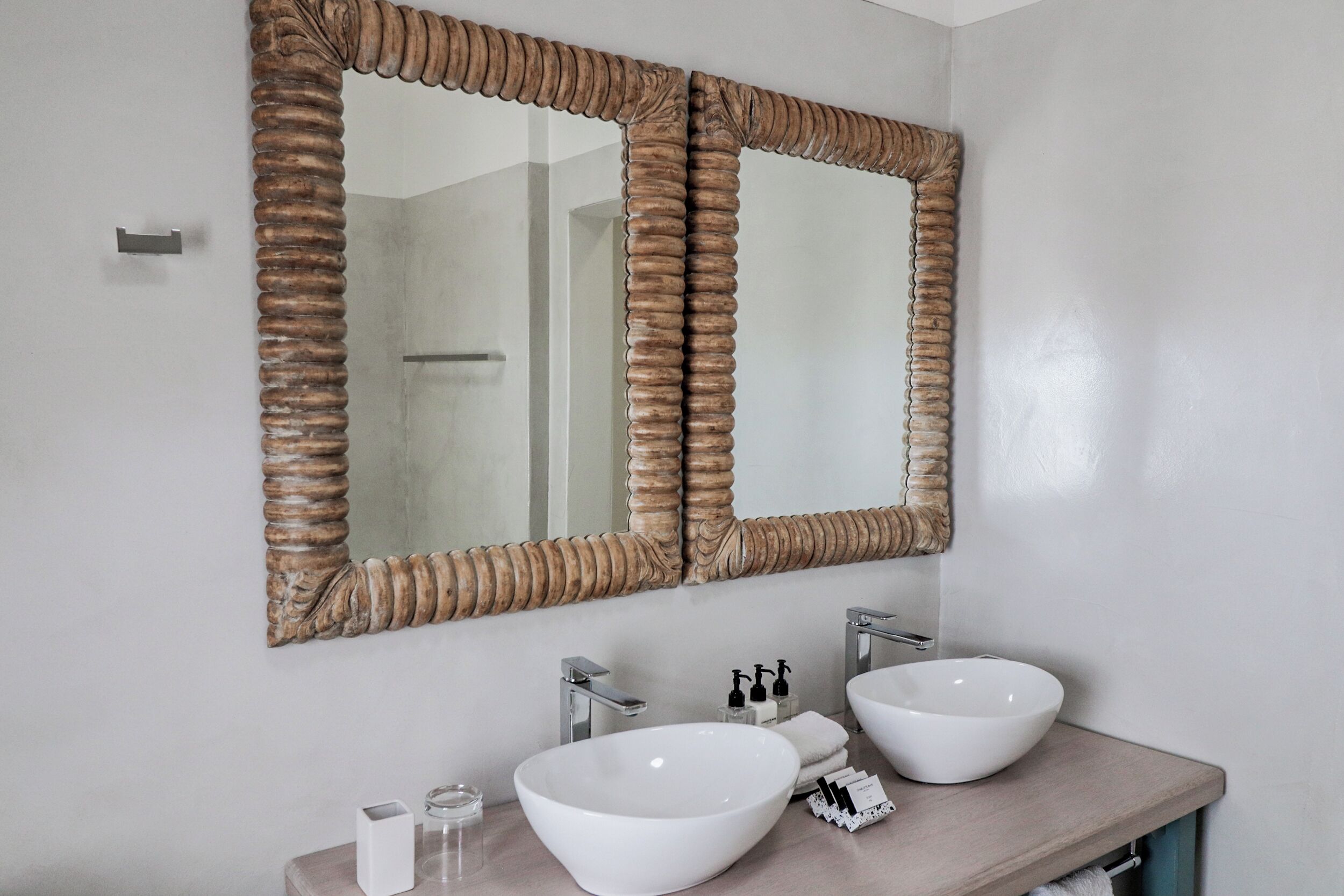 A bathroom with two white vessel sinks, a large mirror with a wooden frame, and a towel rack.