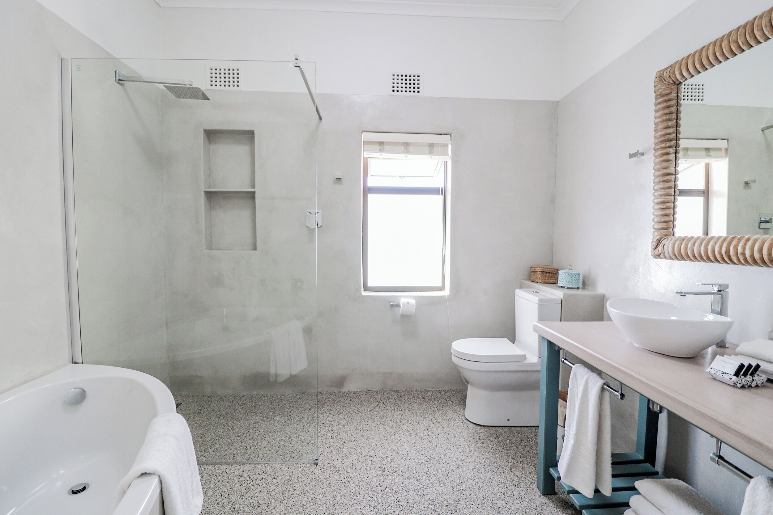 Un baño moderno con ducha envuelta en cristal, una bañera blanca, un lavamanos con un espejo grande y un inodoro.