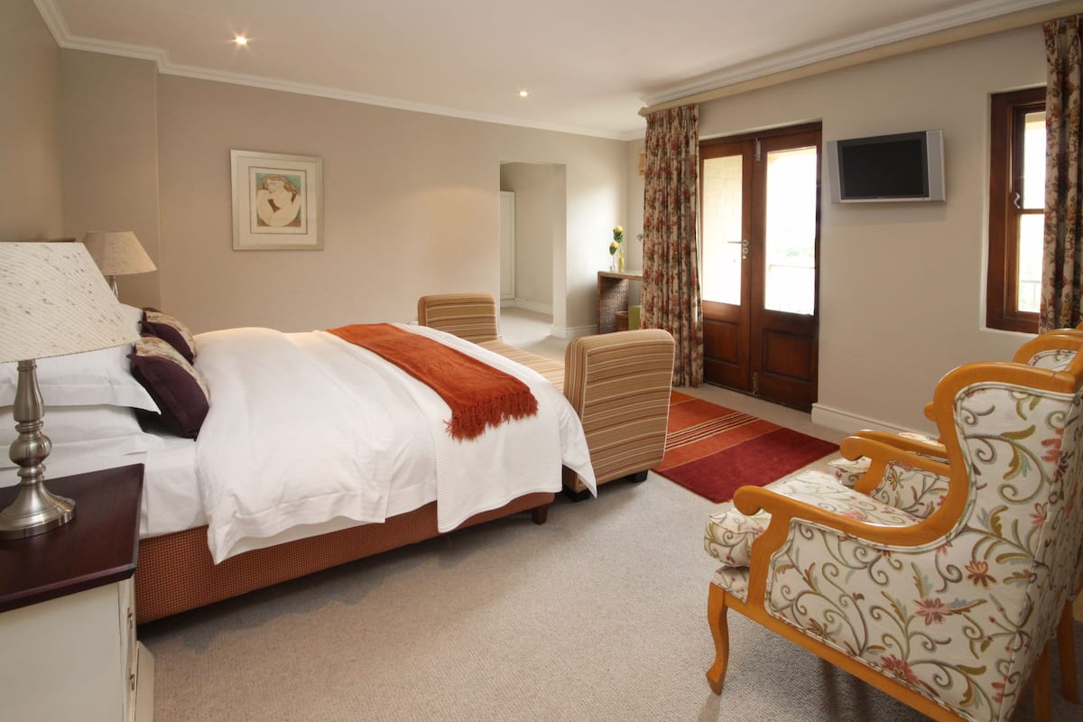 Une chambre d’hôtel avec un grand lit, une chaise, un bureau, une télévision et une fenêtre avec des rideaux.