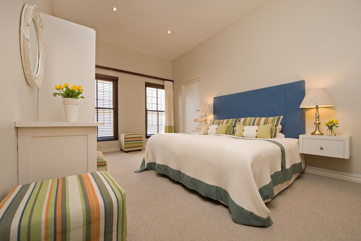 Une chambre à coucher avec un lit, des tables de chevet, une lampe, un miroir et une fenêtre avec des stores.