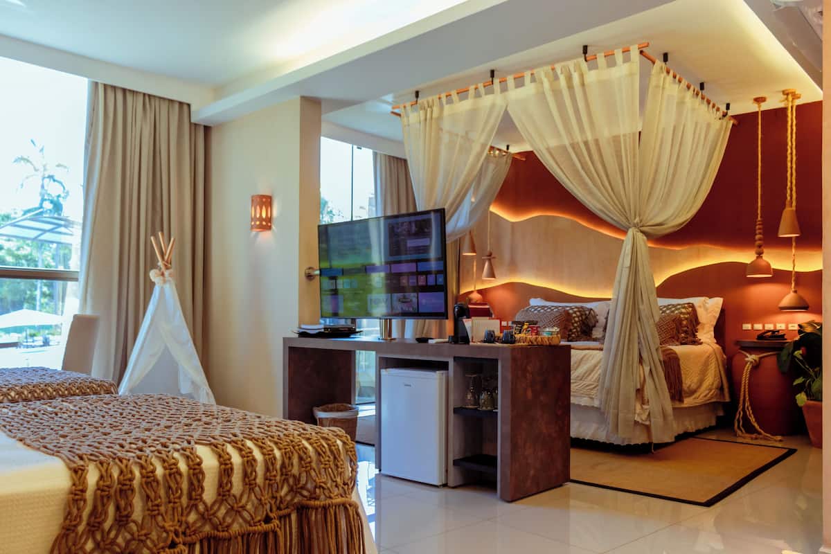 Una habitación de hotel moderna con una cama, un escritorio con ordenador, televisor y un refrigerador pequeño.