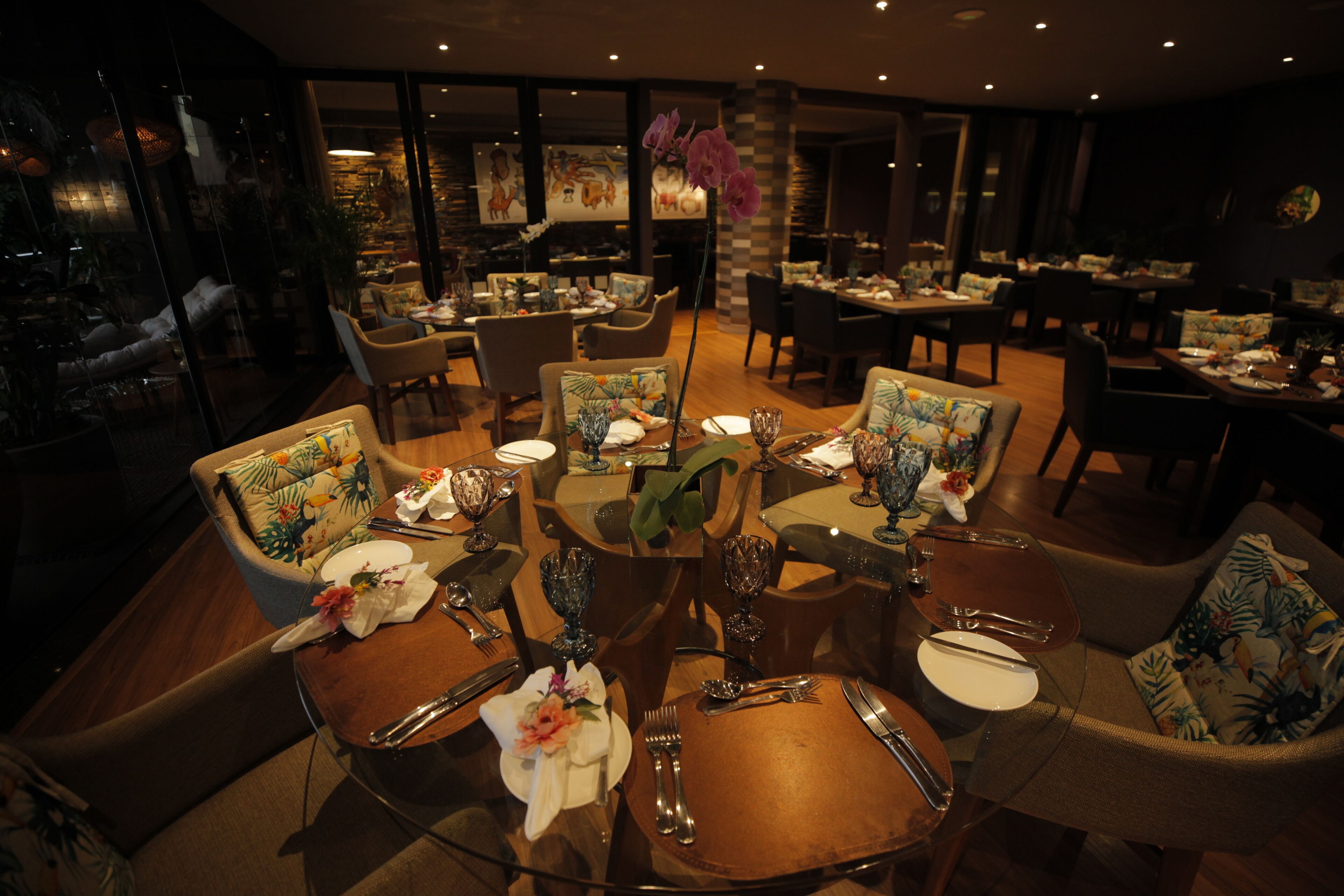 Un restaurant avec des tables rondes, des chaises recouvertes d’un tissu à motifs floraux et une ambiance chaleureuse.