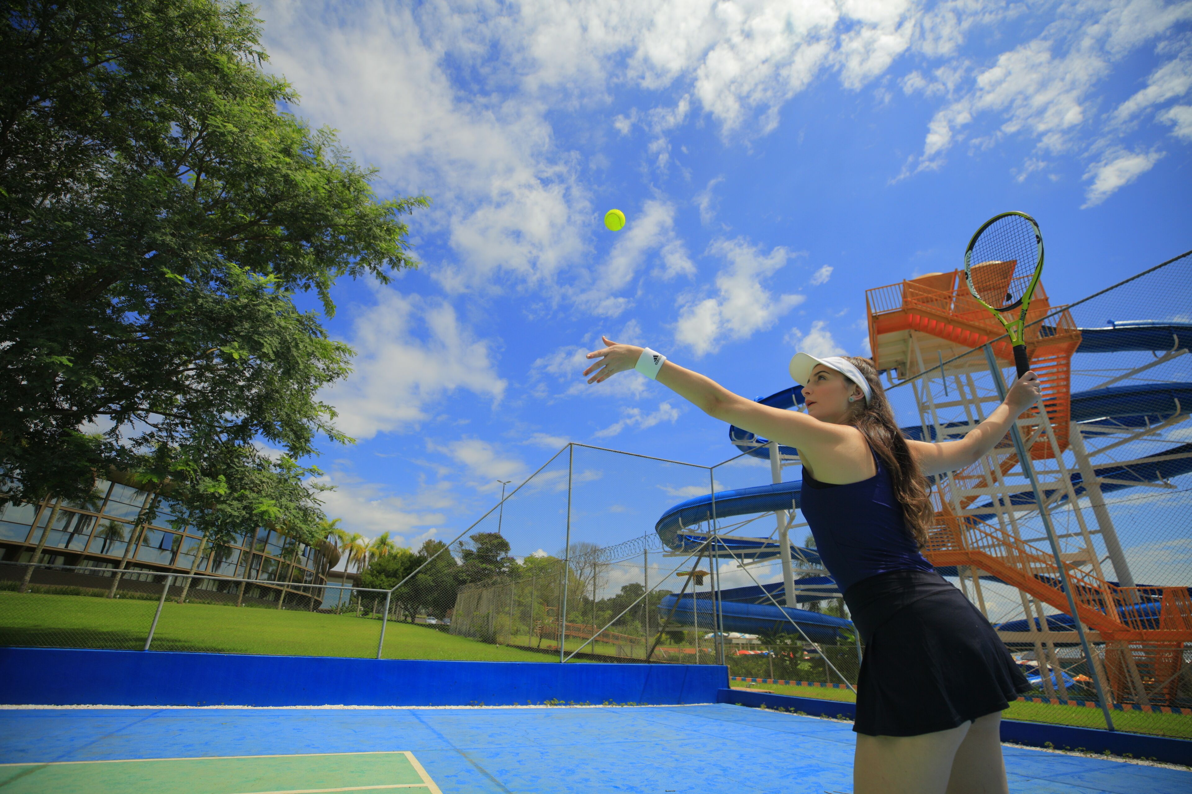 A tennis court with a blue surface, surrounded by a fence and trees.