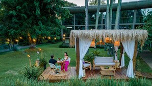 Un área de comedor al aire libre con techo de paja, mobiliario de madera y luces colgantes.
