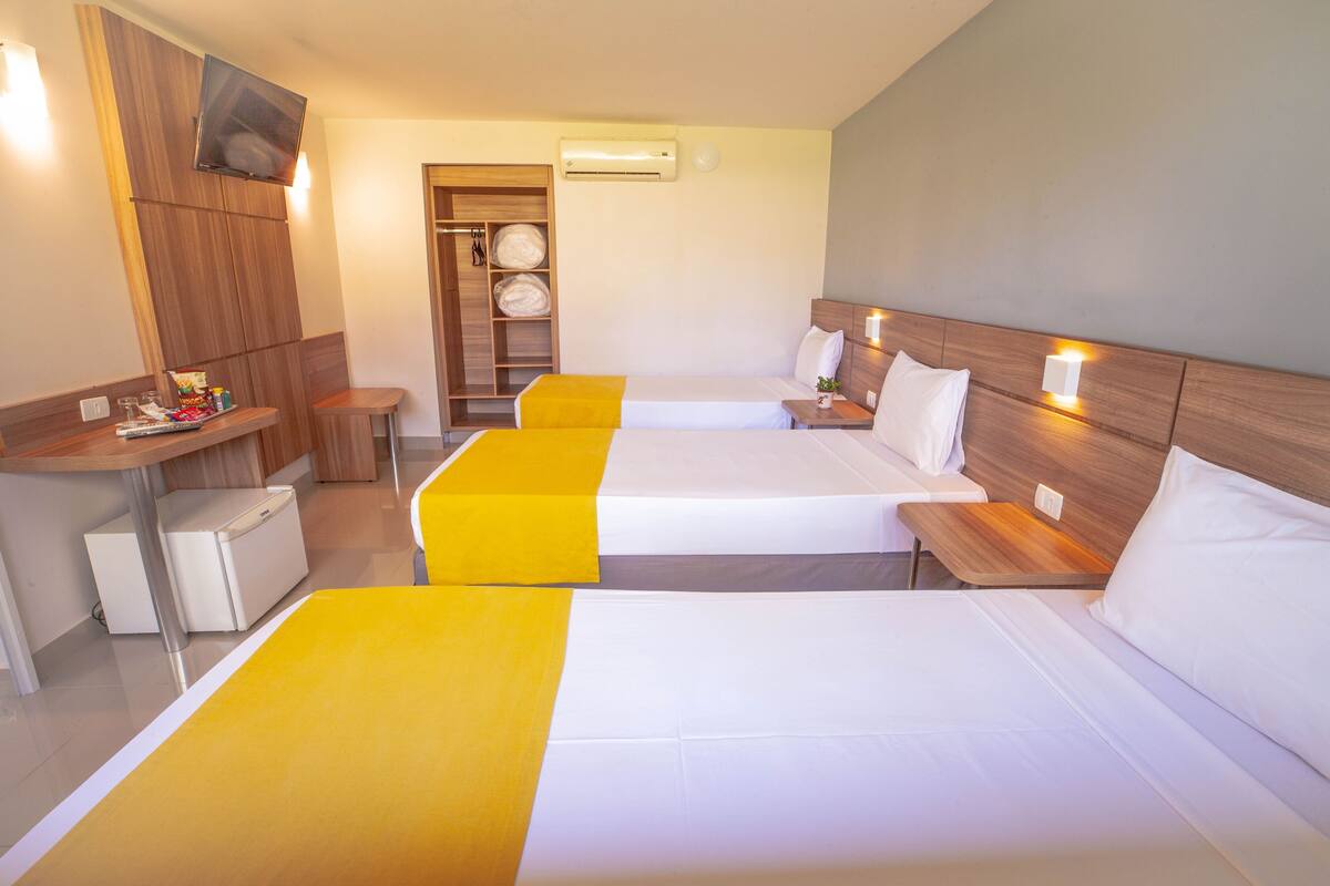 Ein Hotelzimmer mit drei Betten, einem Schreibtisch, einem Kleiderschrank und einem Fernseher.