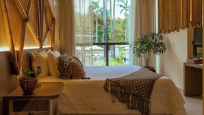 A hotel room with a large bed, a bedside table with a plant, a view of palm trees, and a bamboo wall design.