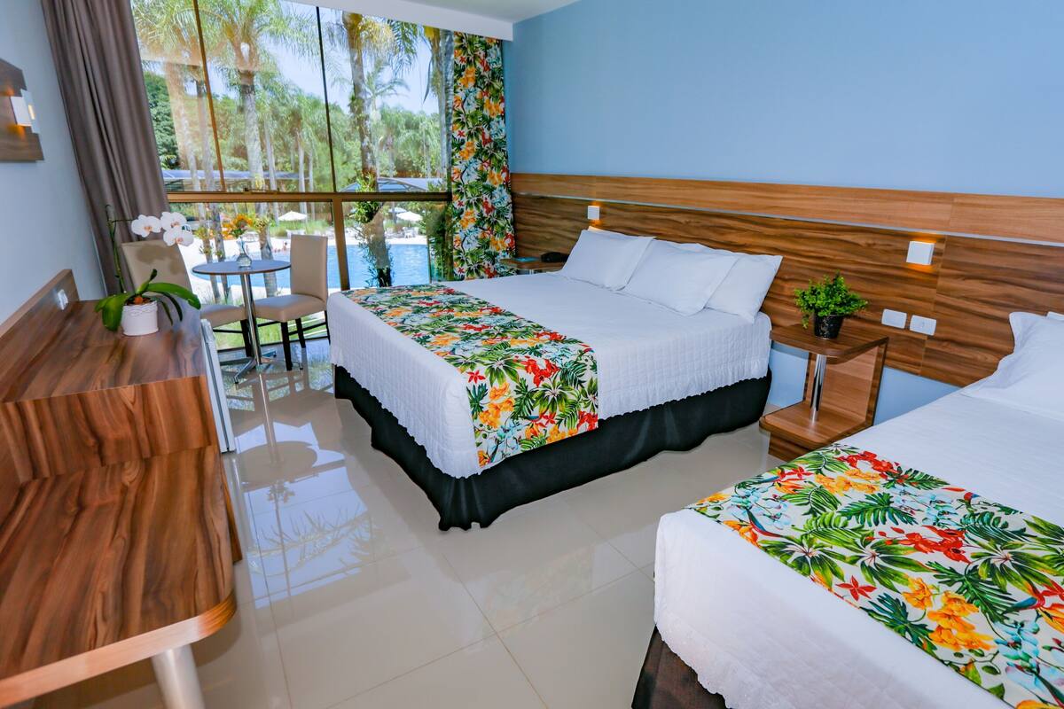 Habitación de hotel con dos camas, un escritorio de madera y vistas a una piscina y palmeras.