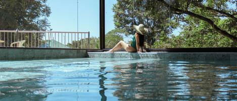 Una persona sentada junto a una piscina, con vistas a árboles y un cielo despejado.
