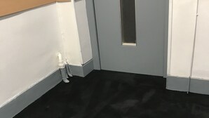A room with a black carpet, white walls, and a door with a small window. - Hôtel Océan (Lourdes)