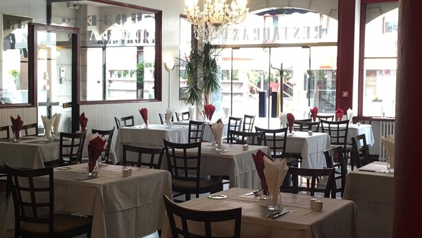 A restaurant with multiple tables and chairs, a chandelier, and large windows with a view of the street. - Hôtel Océan (Lourdes)