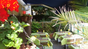 An outdoor patio with tables set for dining, surrounded by greenery and plants. - Hôtel Océan (Lourdes)