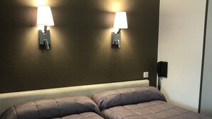 A double bed with a grey quilted cover, two wall-mounted lamps, and a telephone on the wall. - Hôtel Océan (Lourdes)