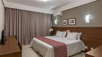 A hotel room with a bed, a desk, a chair, an air conditioning unit, and a wall-mounted light.