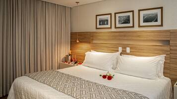 Quarto de hotel com uma cama grande, cabeceira de madeira e três quadros na parede.