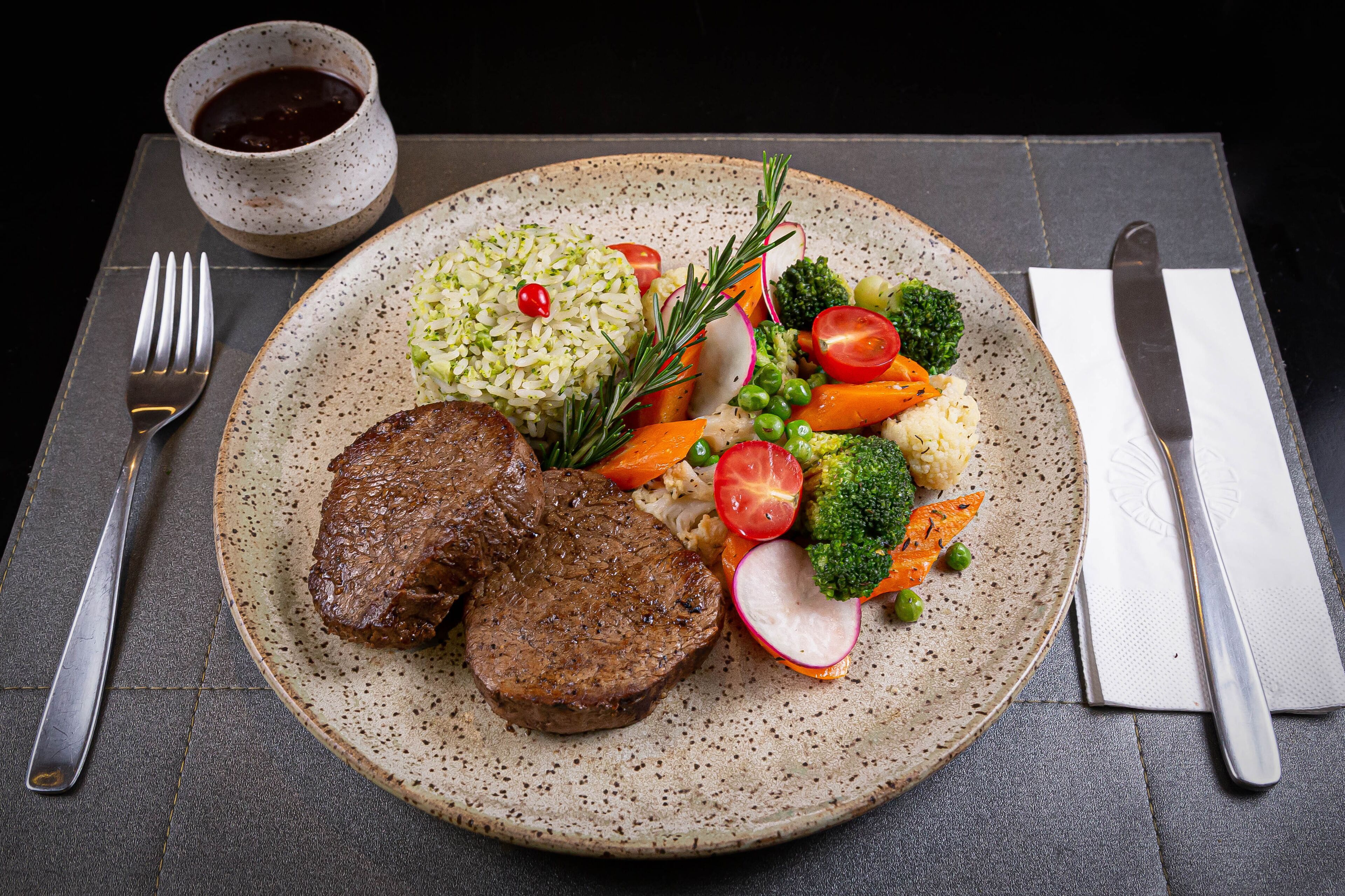Prato com bife, arroz e legumes sobre um prato de cerâmica texturizado.