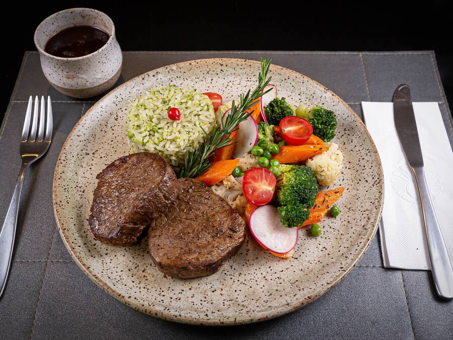 A plate with steak, rice, and vegetables on a speckled ceramic plate.