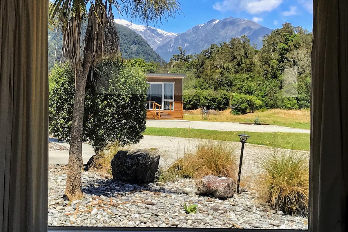 Un edificio moderno con fachada de vidrio, rodeado de un paisaje natural con árboles y una montaña al fondo.