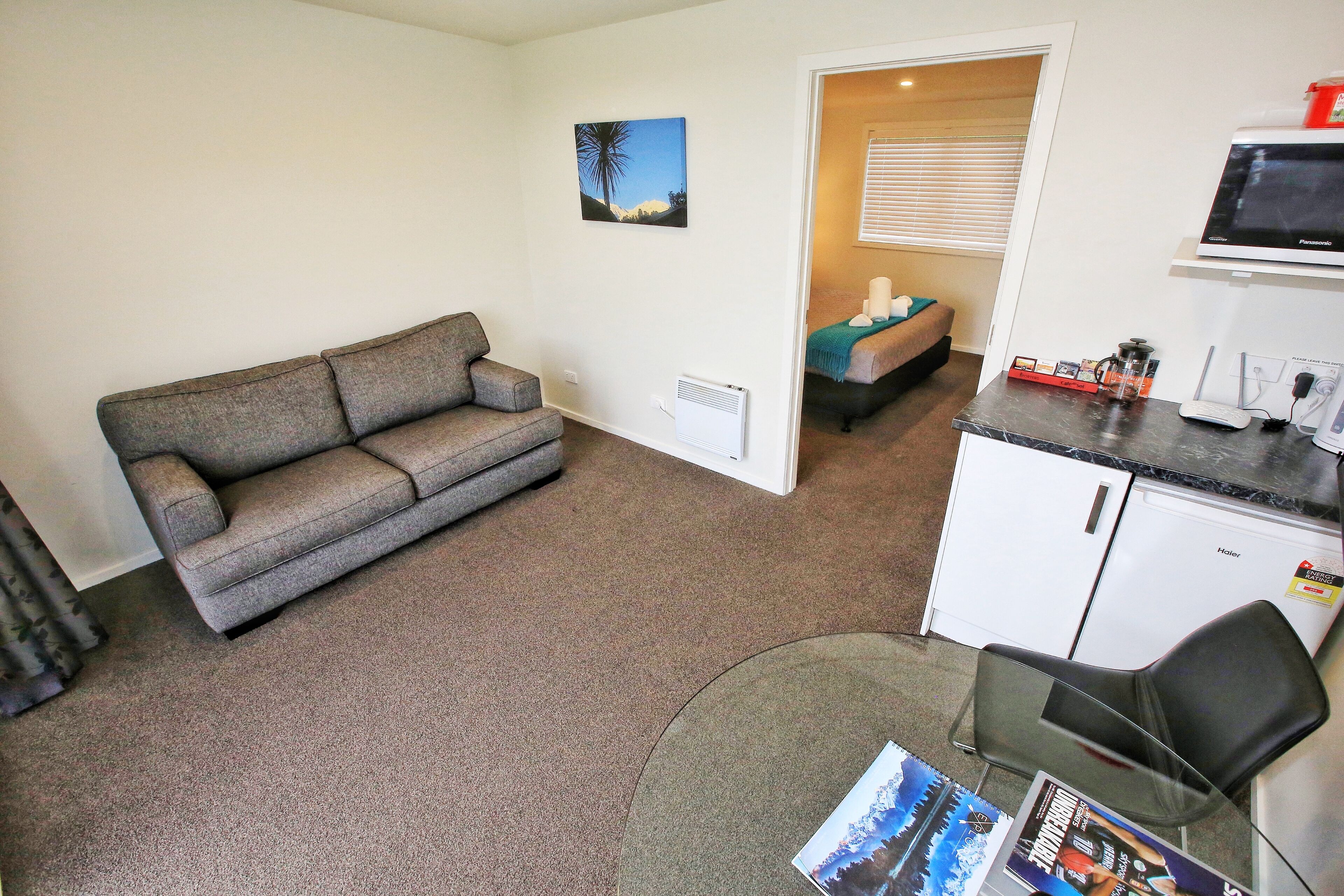A compact living space with a sofa, a small kitchenette, a dining area, and a door leading to another room.