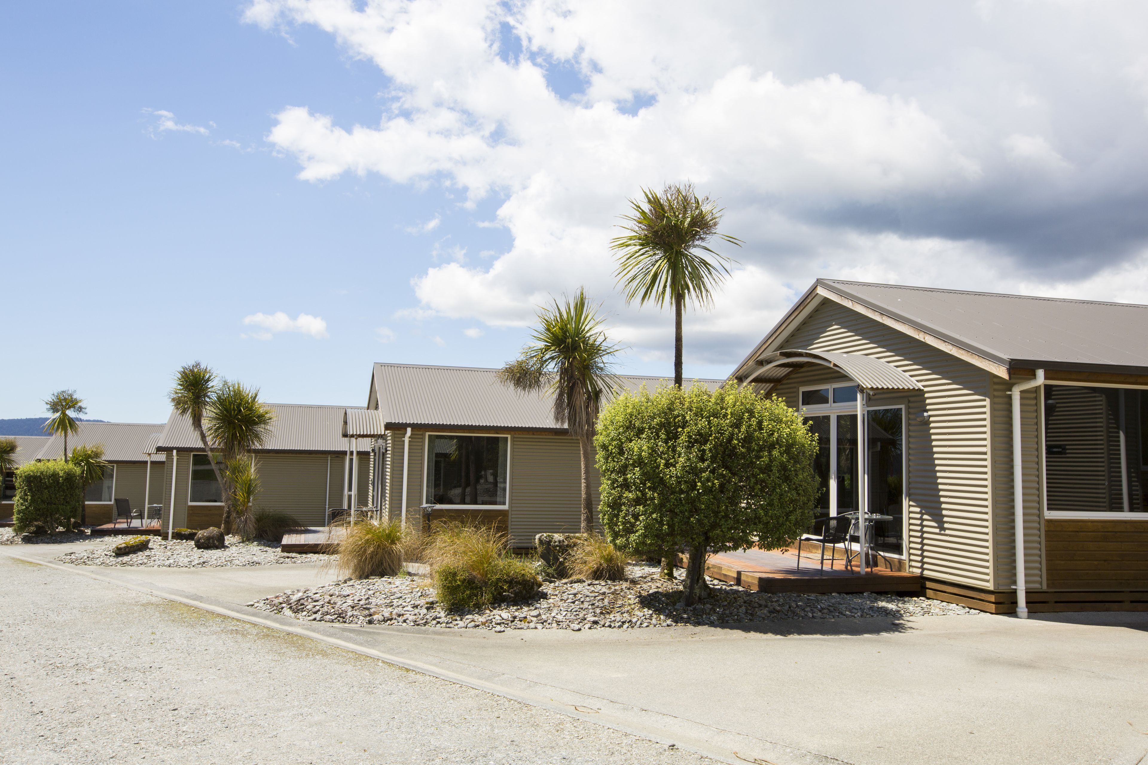 A row of modern, single-story buildings with a flat roof, each featuring a patio area with outdoor seating.