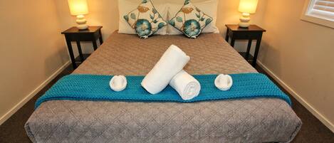 A neatly made bed with a blue blanket, two pillows with floral patterns, and two bedside lamps.