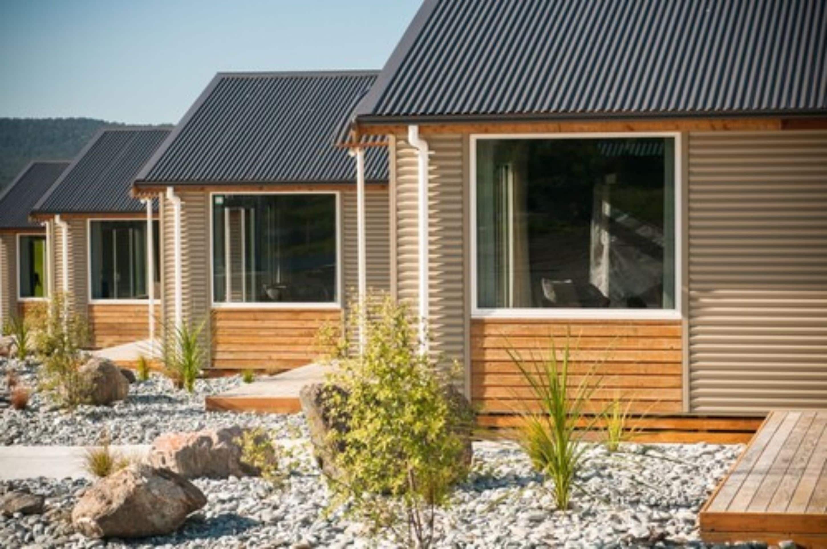 A row of modern cabins with large windows, wooden decks, and a rocky landscape.