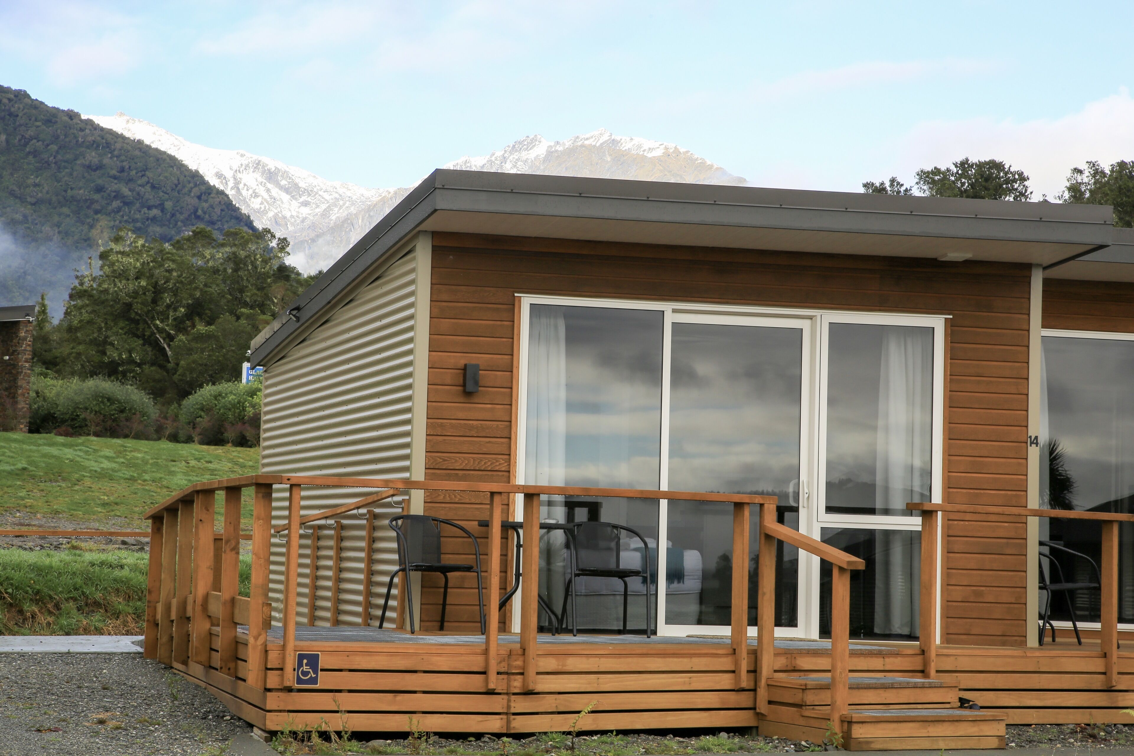 A wooden cabin with a deck, large sliding glass doors, and a wheelchair-accessible ramp.