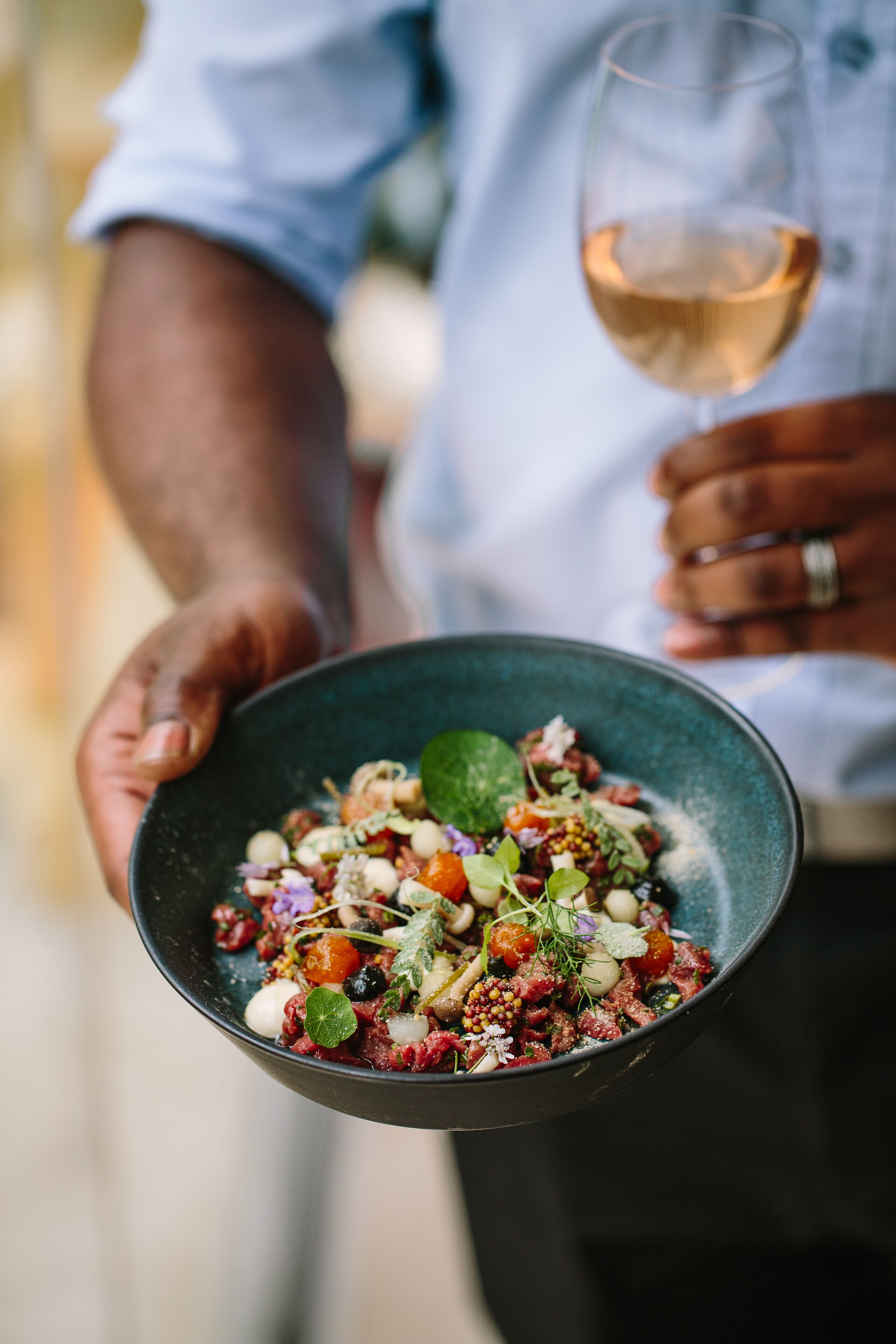Una persona sosteniendo un tazón de ensalada y una copa de vino.