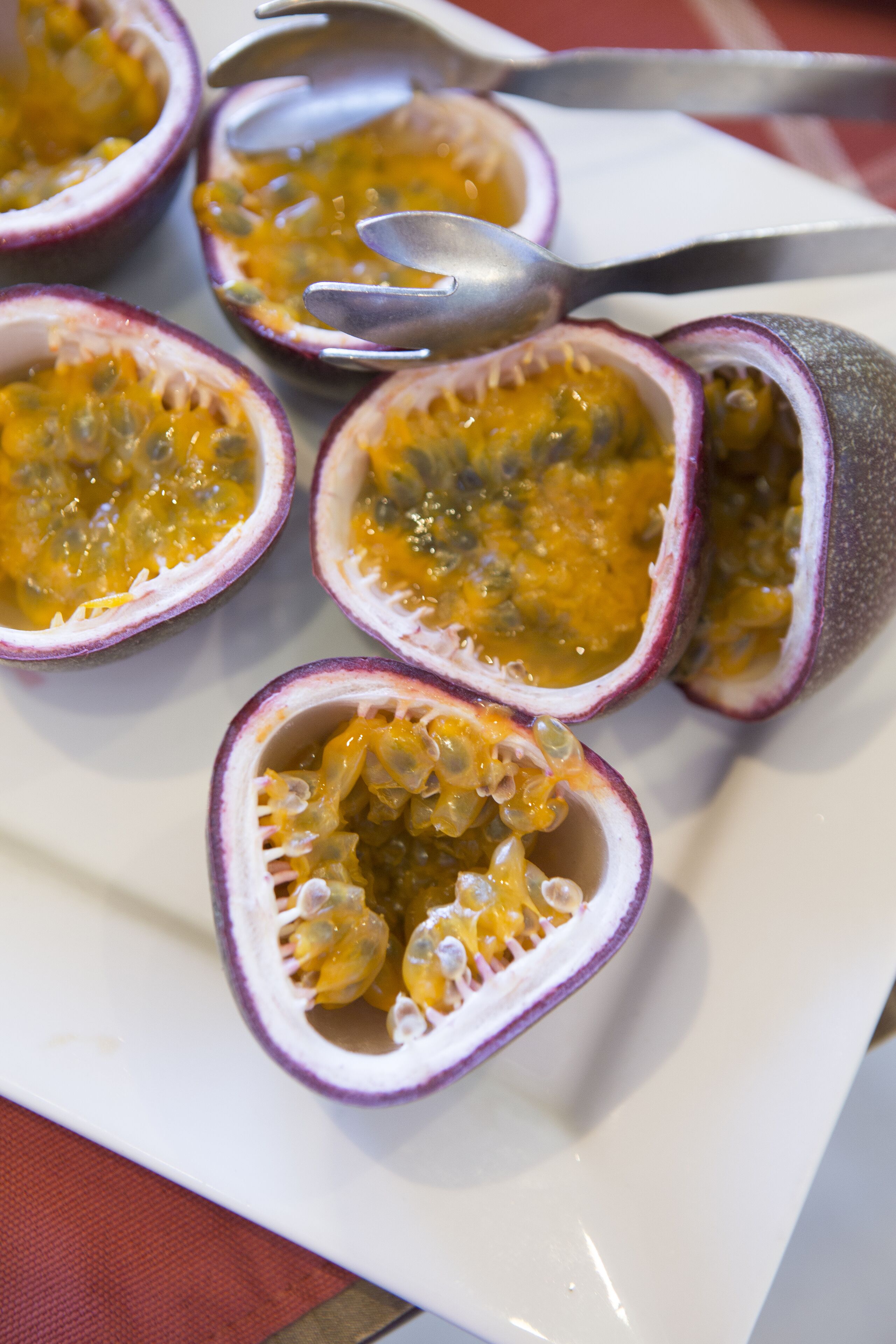 A plate with several halves of passion fruit, some cut open to reveal the seeds and pulp.