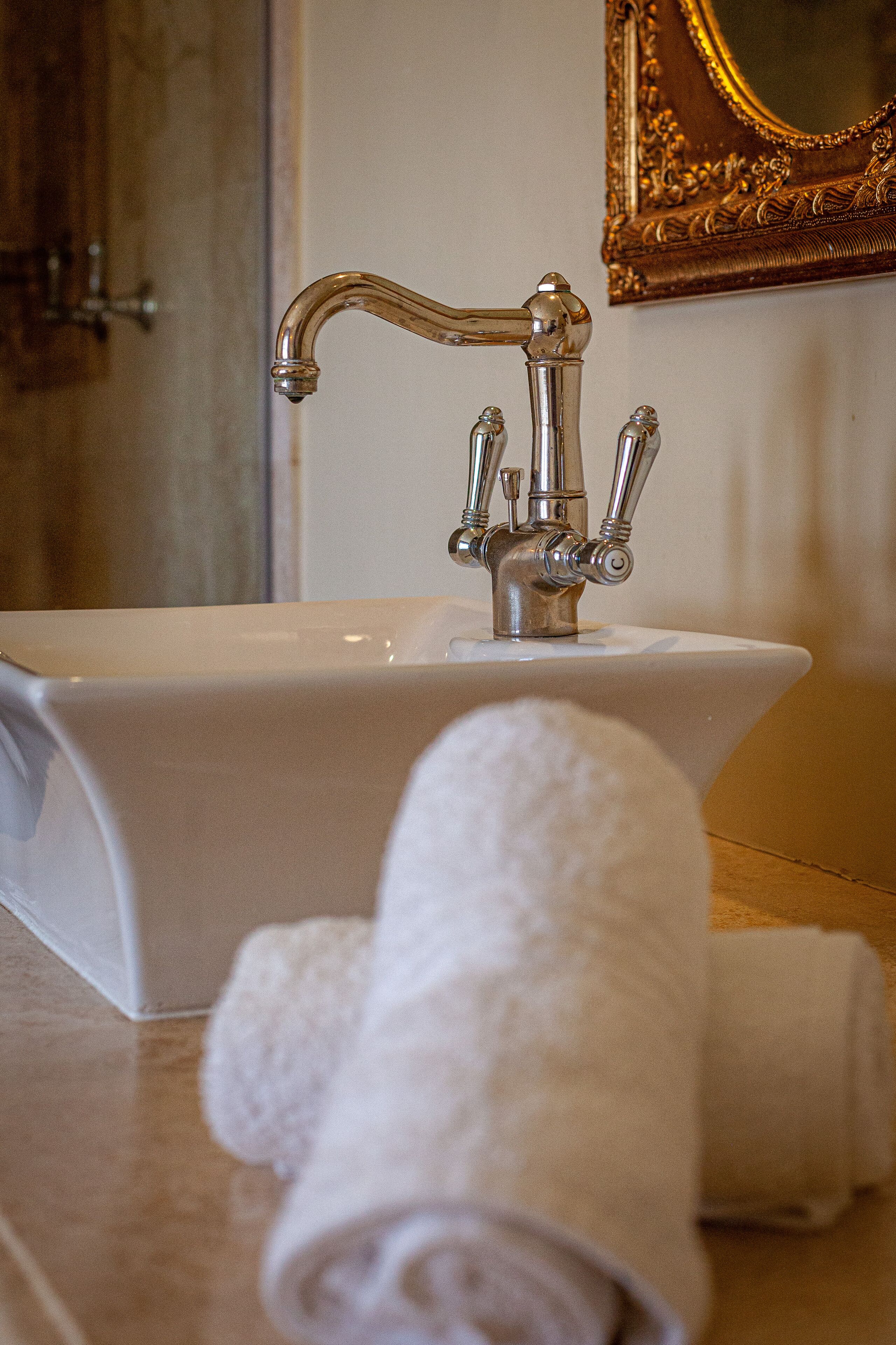 A bathroom with a white sink, a gold-framed mirror, and rolled towels on the counter.