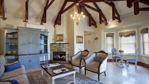A spacious living room with a fireplace, wooden beams, and a chandelier. There is a sofa, chairs, and a coffee table. - Franschhoek Country House and Villas (Franschhoek)