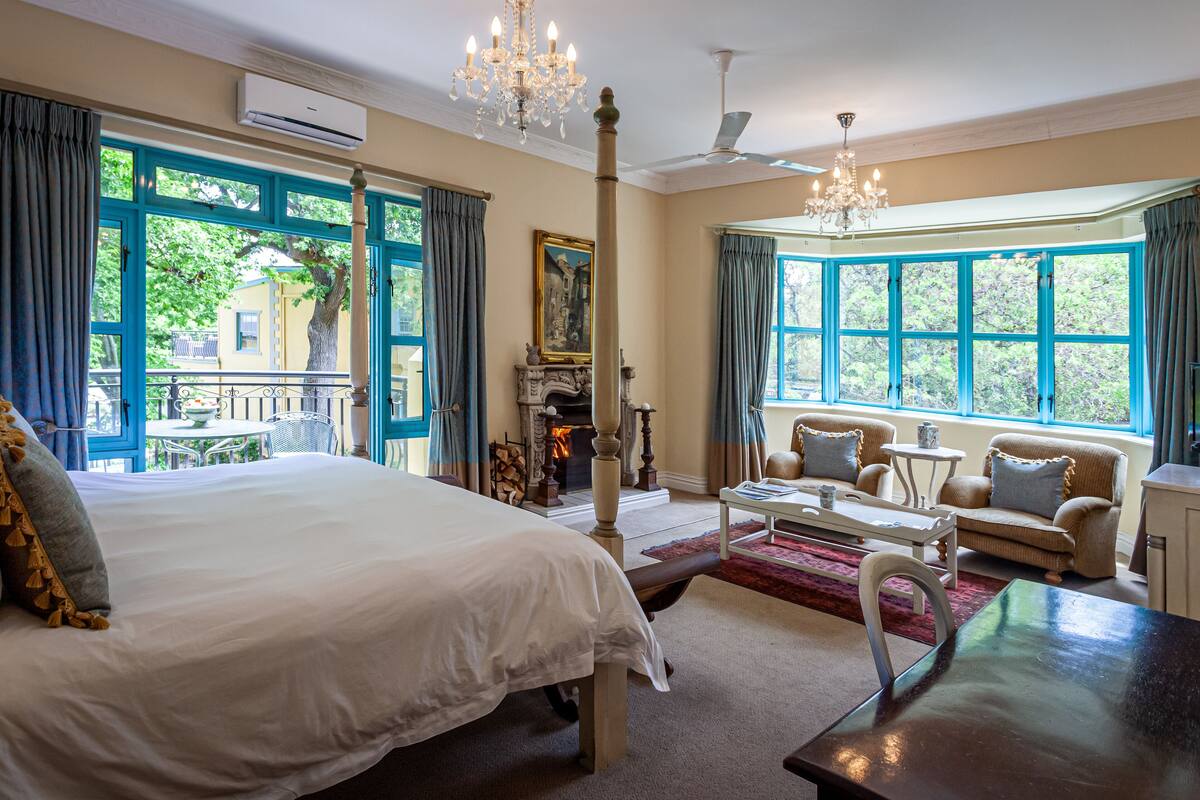 Een ruime slaapkamer met een groot bed, een open haard, een eethoek en uitzicht op de omgeving.