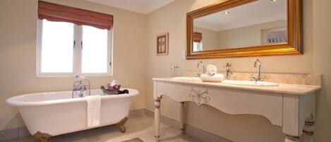 A bathroom with a freestanding bathtub, a vanity with a mirror, and a window with a red valance.