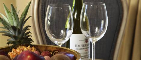 A dining table with a fruit bowl, two wine glasses, a bottle of wine, and a chair.