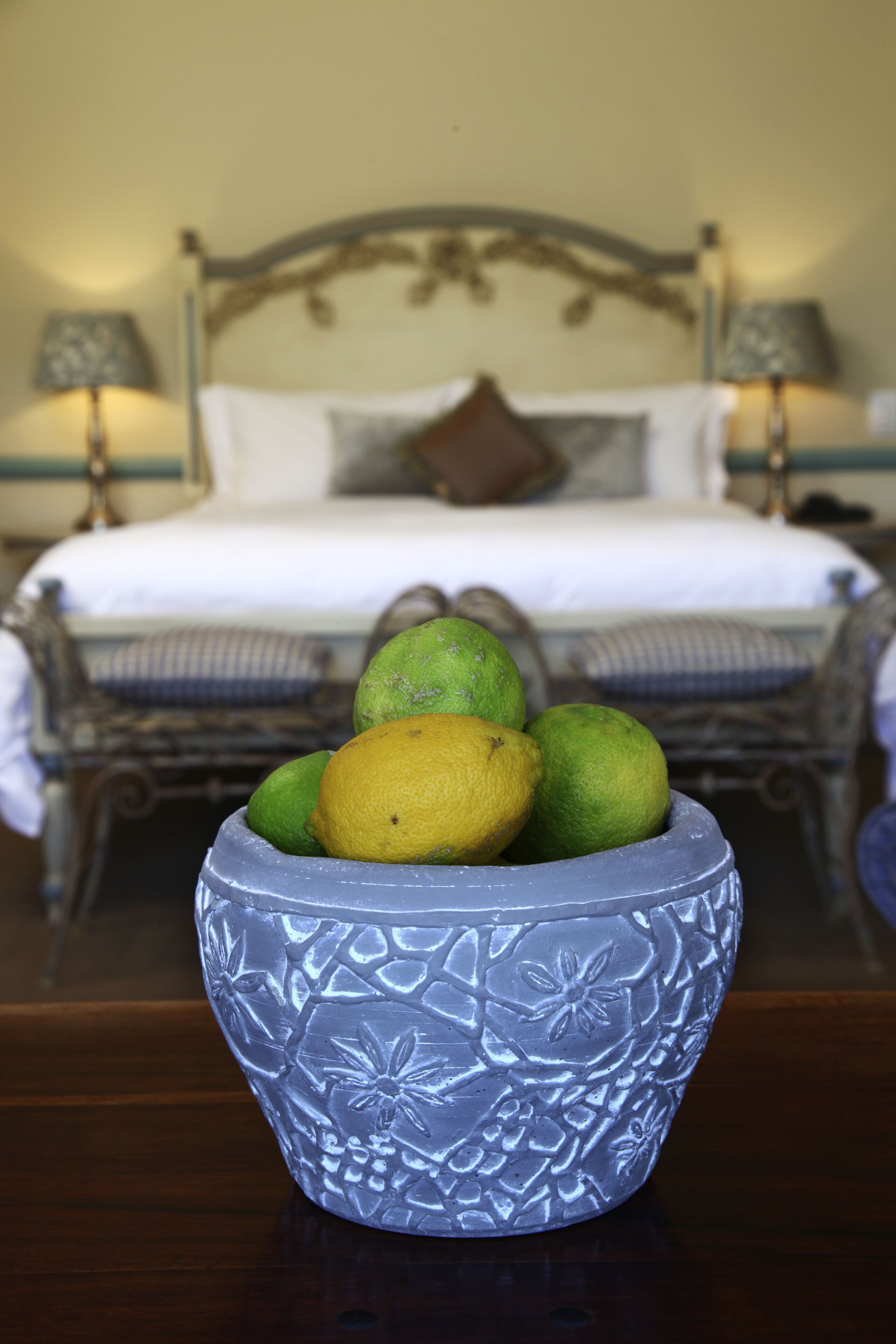 A bed with a headboard, a bedside table with a lamp, and a bowl of fruit on the table.
