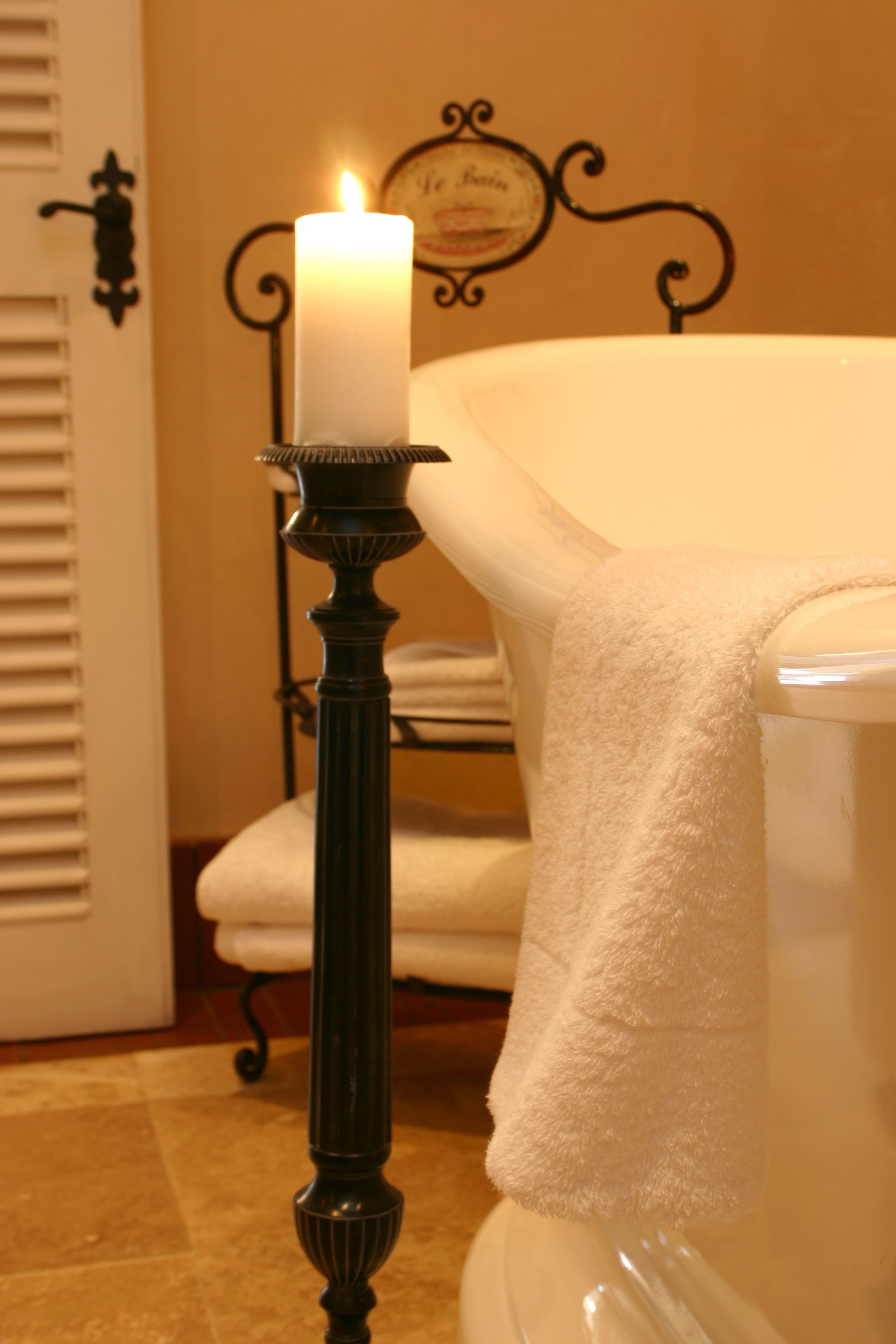 A bathroom with a white bathtub, a lit candle on a black pedestal, and a towel rack with folded towels.