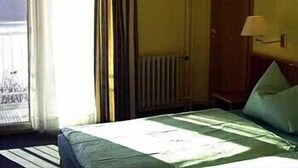 Hotellihuone, jossa on sänky, ikkuna verhoilla, patteri ja puinen vaatekaappi.