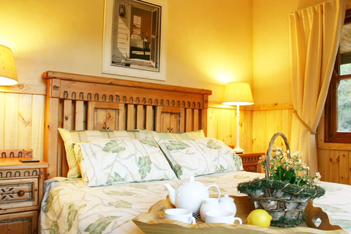Ein gemütliches Schlafzimmer mit einem Holzkopfteil, floralem Bettbezug, Nachttischlampen, einem gerahmten Bild und einem Nachttisch mit Lampe und einer Blumenkorb.