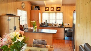 Une cuisine aux murs lambrés, équipée d’une cuisinière, d’un réfrigérateur et de meubles de rangement en bois. Il y a une horloge au mur et un vase rempli de fleurs sur le comptoir.