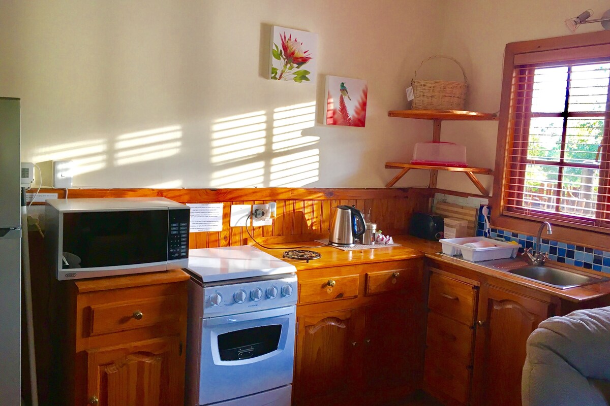 Eine Küche mit Holzausstattung, einer Mikrowelle, einem Backofen, einem Wasserkocher und einem Fenster mit Jalousien.