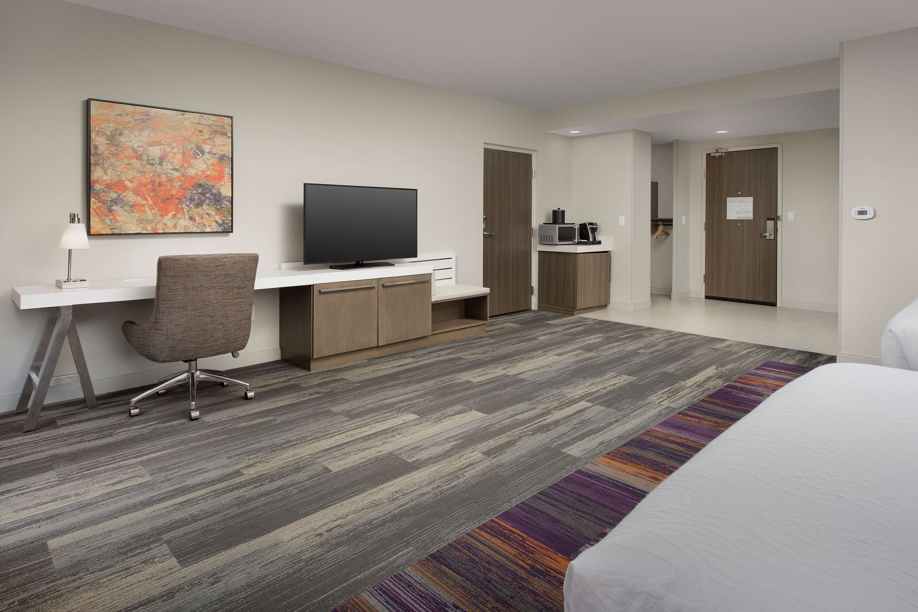 A modern hotel room with a flat-screen TV, a desk, a comfortable chair, a bed, and a microwave.