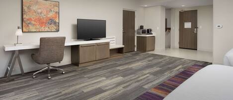A modern hotel room with a flat-screen TV, a desk, a comfortable chair, a bed, and a microwave.