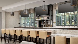 A modern bar area with a marble countertop, multiple bar stools, and a large flat-screen TV mounted on the wall.
