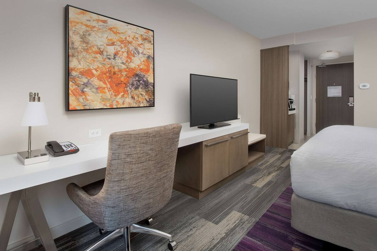 Una camera d'albergo con scrivania, sedia, televisore, letto e un grande quadro astratto appeso al muro.