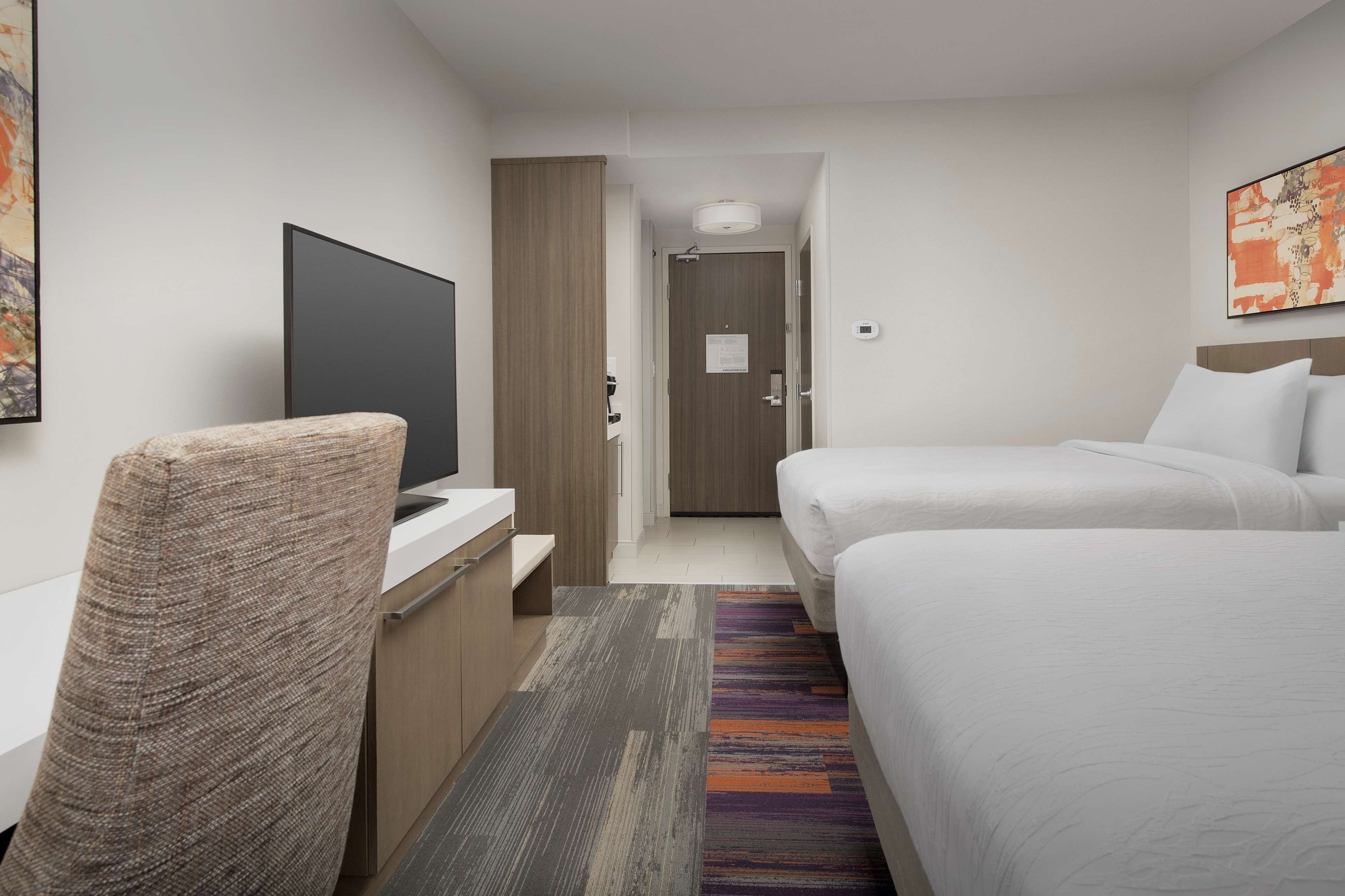 Habitación de hotel con cama, escritorio con silla, televisor y puerta que da a otra habitación.
