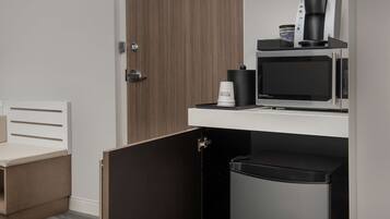 A compact kitchenette with a coffee maker, microwave, and a small trash bin.