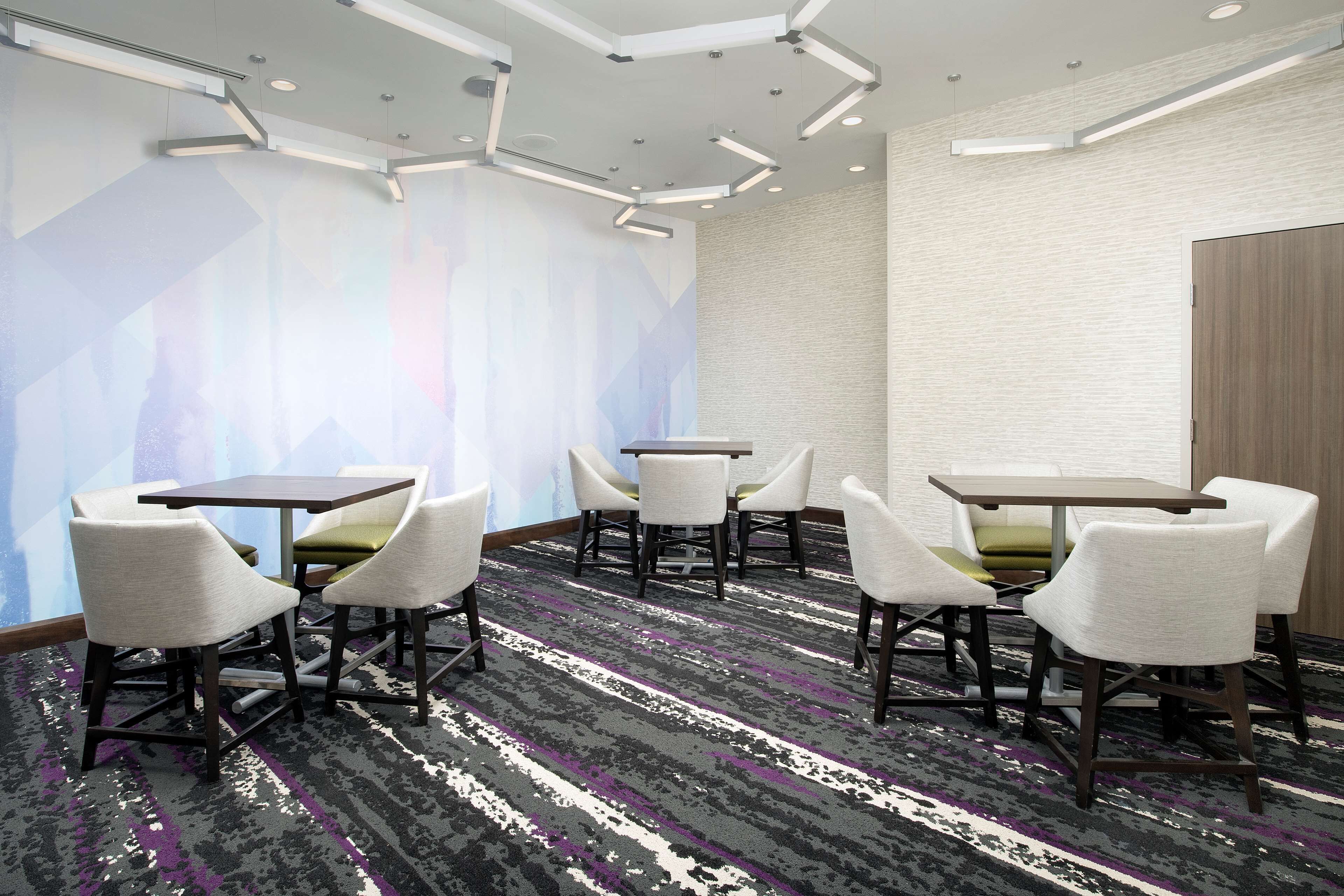 Une salle de conférence au design moderne, dotée d’un tapis à motifs, de chaises blanches et vertes, et d’un grand mur orné d’œuvres d’art abstraites.