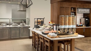 A modern kitchen with a central island, bar stools, and a coffee station with various containers.