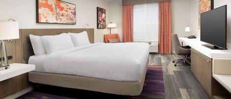 A hotel room with a large bed, a desk with a computer, a TV, and artwork on the walls.