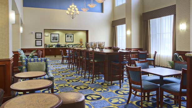 A hotel lobby with a patterned carpet, multiple seating areas including a bar, and a reception desk. - Hampton Inn & Suites Ridgecrest (Ridgecrest)