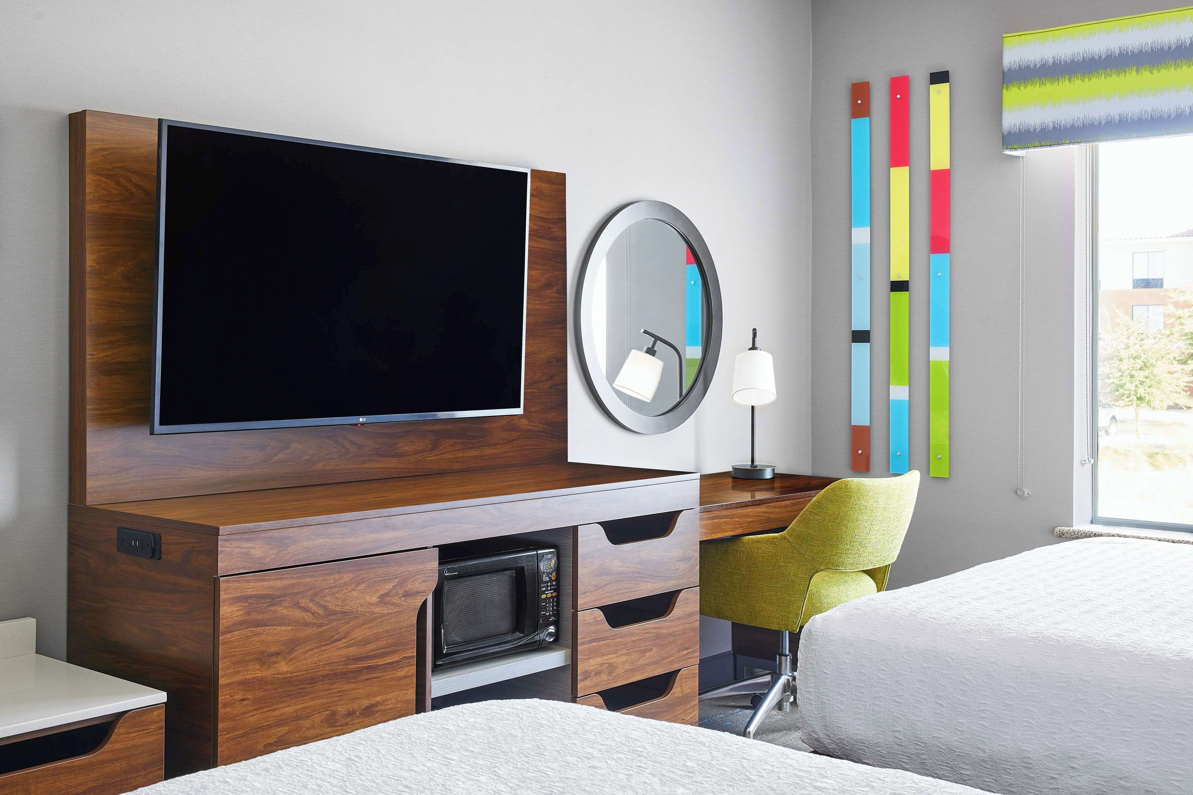 A hotel room with a flat-screen TV, a microwave, a desk with drawers, a chair, and two beds.